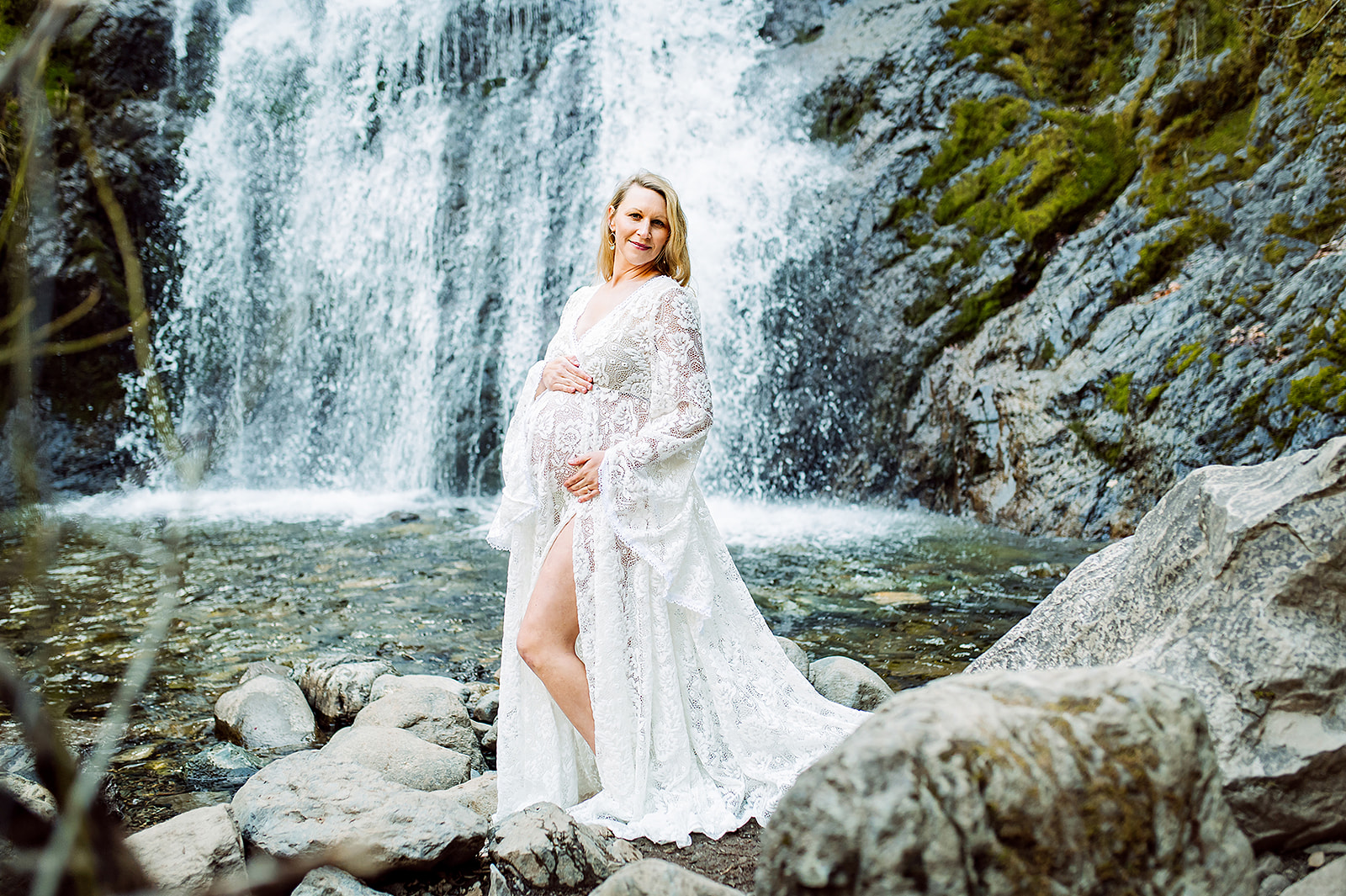 mom to be in a white gown standing in front of a waterfall Be Well Massage Medford