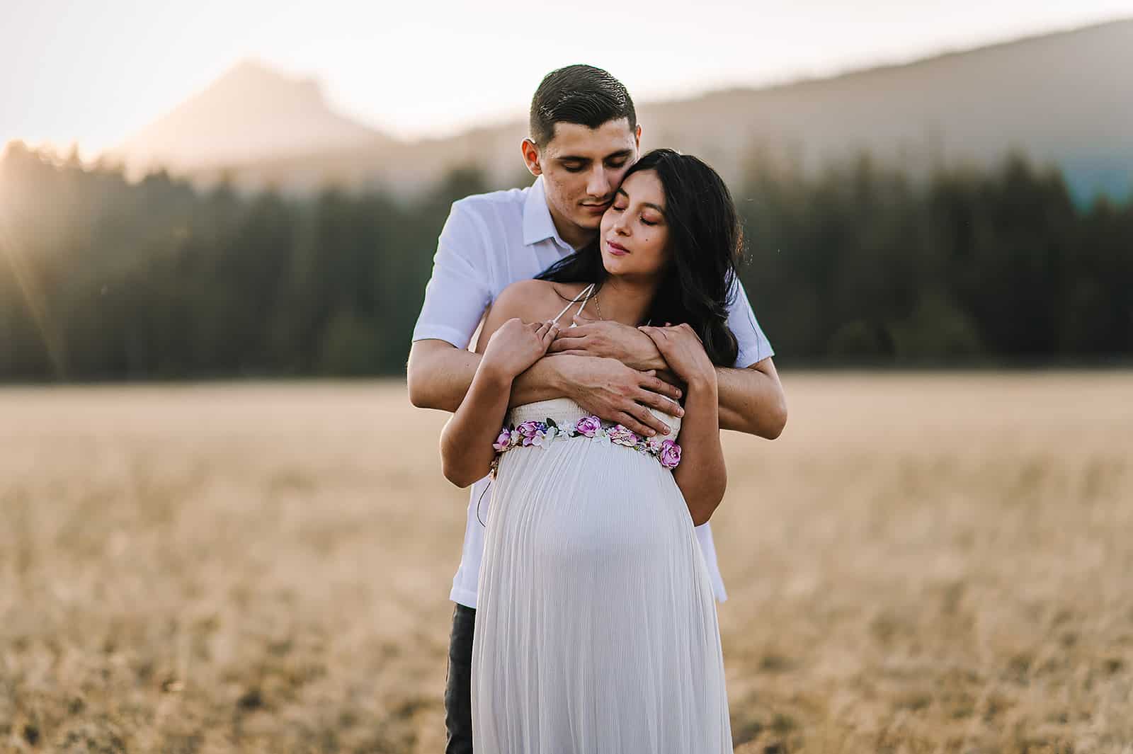 husband hugging mom-to-be in a field Cloud Massage Company