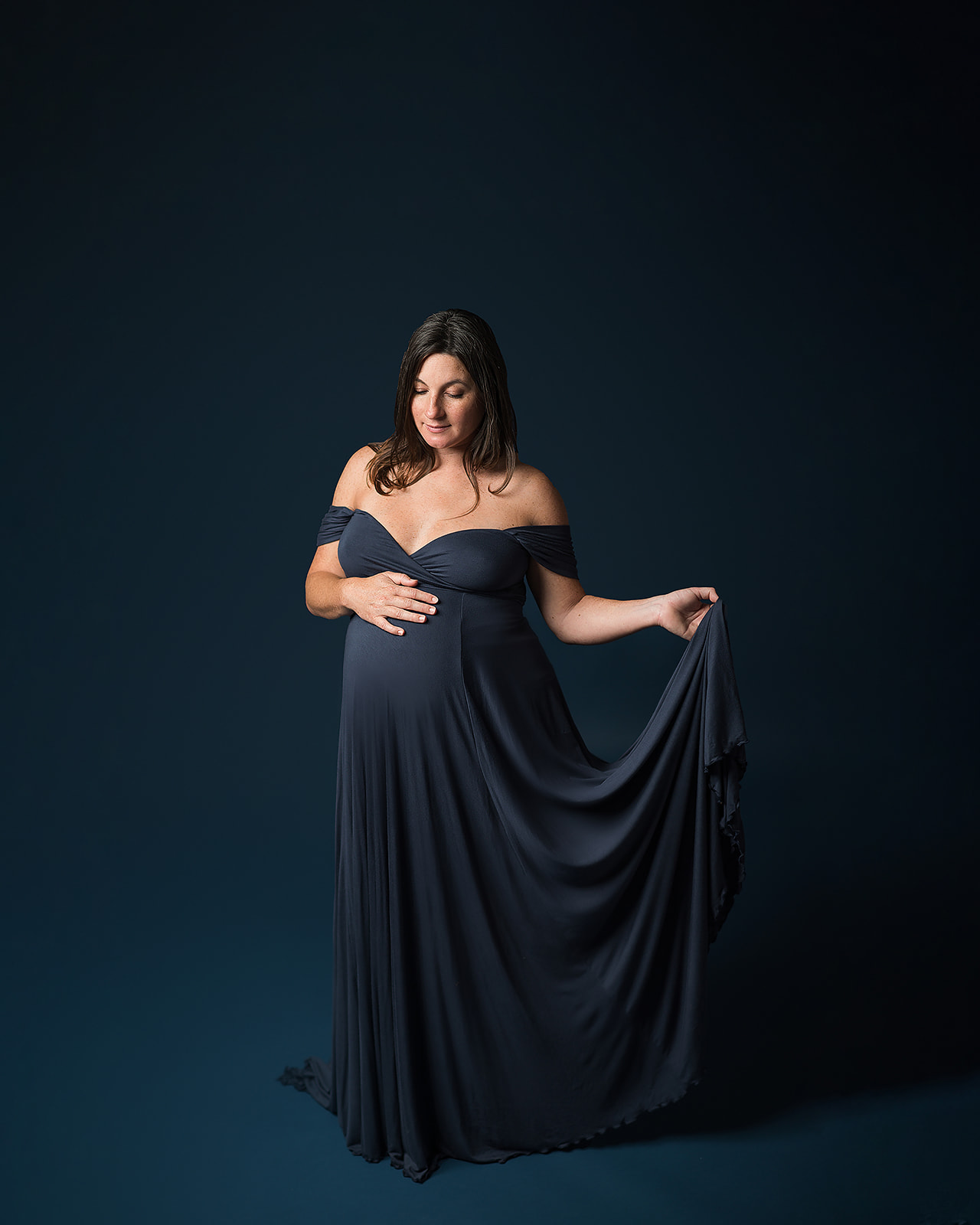 pregnant woman in navy maternity gown holding her train