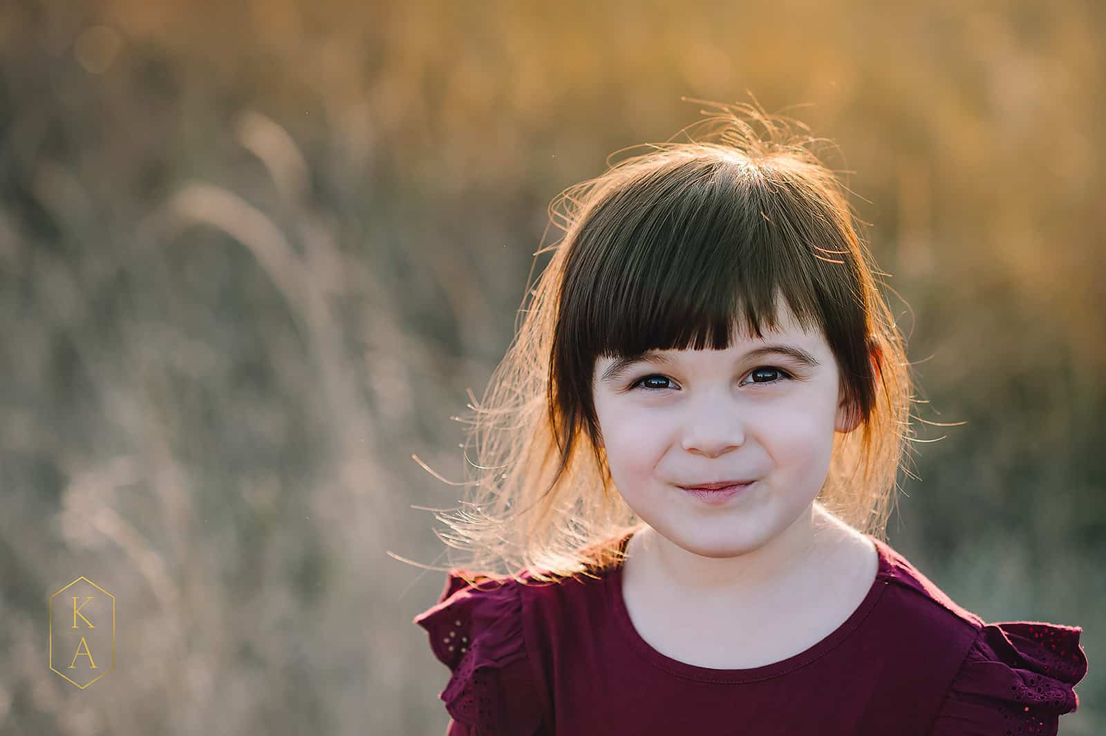 little girl in maroon shirt standing in a field at sunset