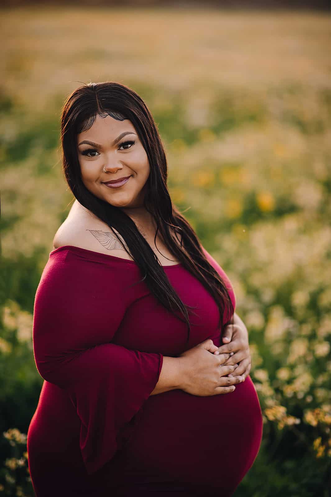 mom to be in maroon maternity gown with her hands on her bump in a field