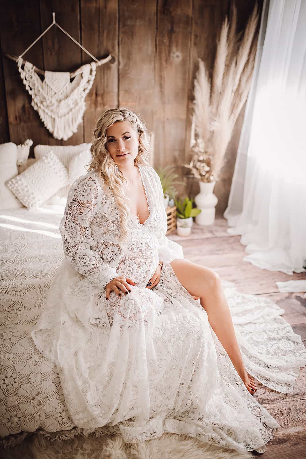 pregnant woman in sheer lace maternity gown sitting at the edge of a white bed Midwives Medford Oregon